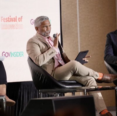 Mohamed Shareef seated on a panel at GovInsider's Festival of Innovation, speaking into a microphone and holding a tablet